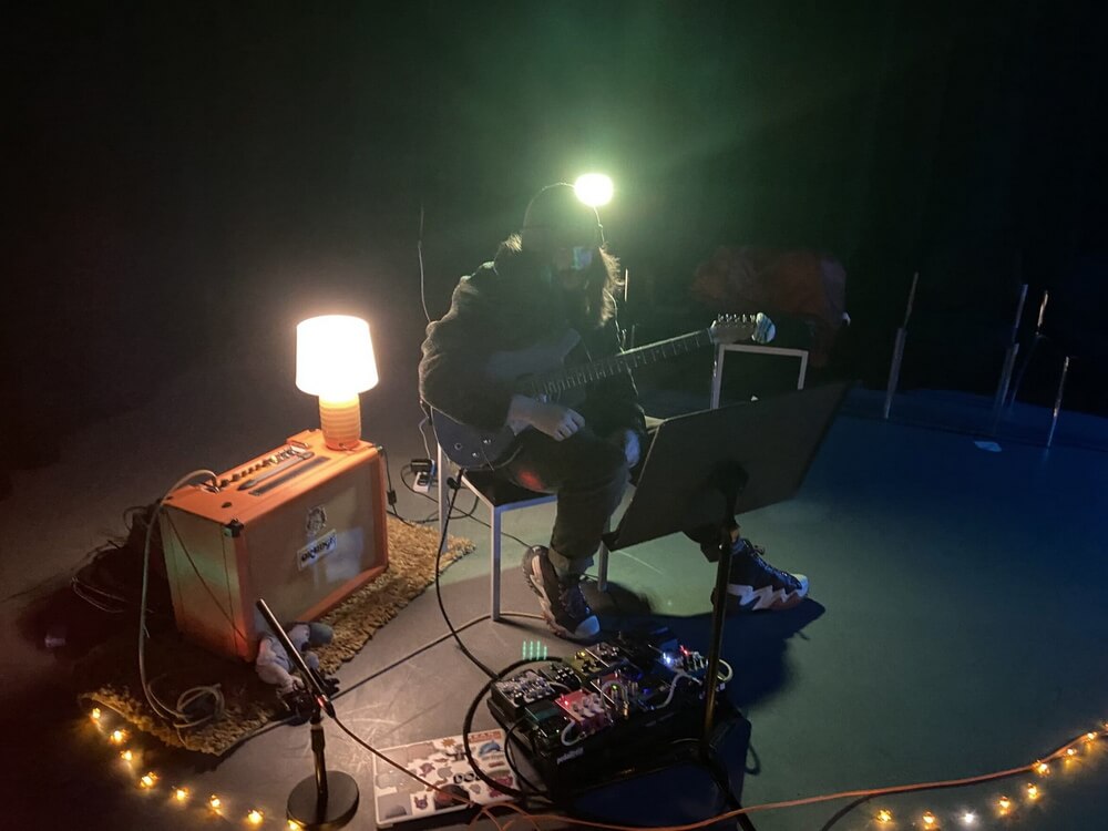 Elliot with guitar, amp and lamp in the performance space
