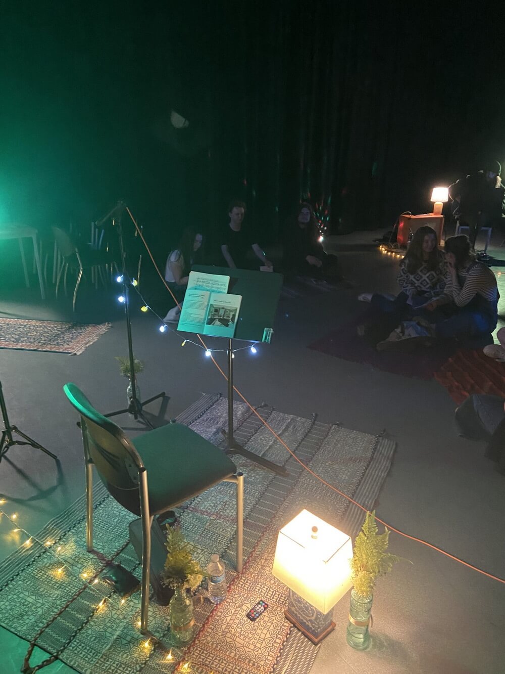 The audience seated on rugs and cushions in the darkened room